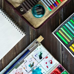 art workplace, color pencils, brushes, watercolor paints, paper crayon pastel chalks