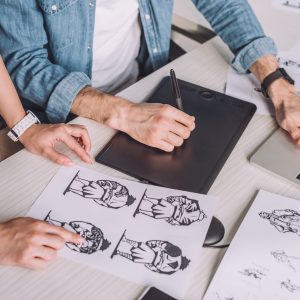 cropped view of illustrator pointing with finger at cartoon sketch near coworker