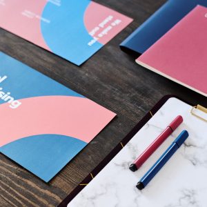 Two highlighters on paper in clipboard surrounded by brochures and copybook