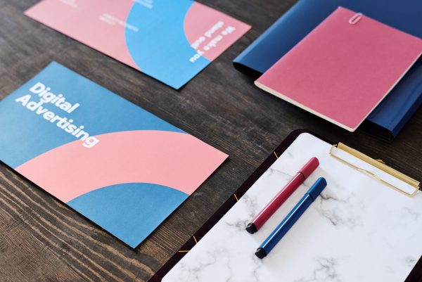 Two highlighters on paper in clipboard surrounded by brochures and copybook